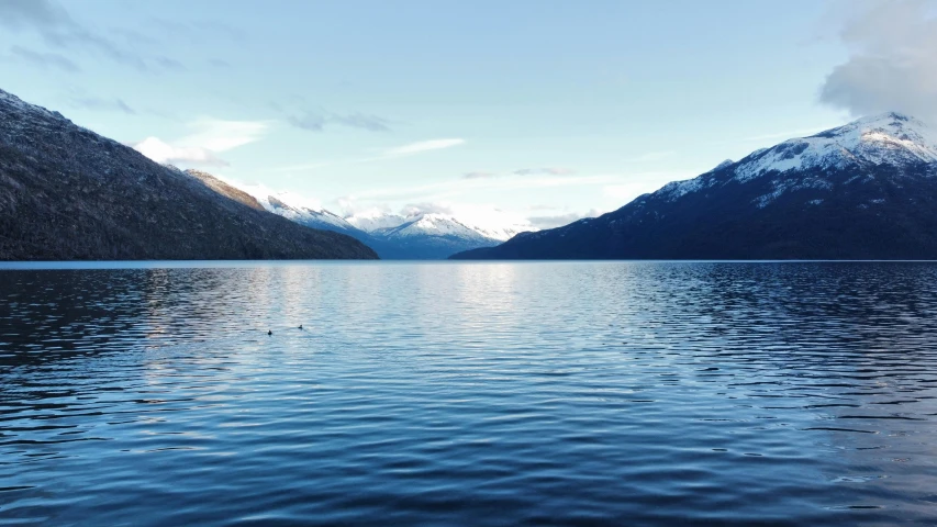 a lake is very calm with mountains in the background