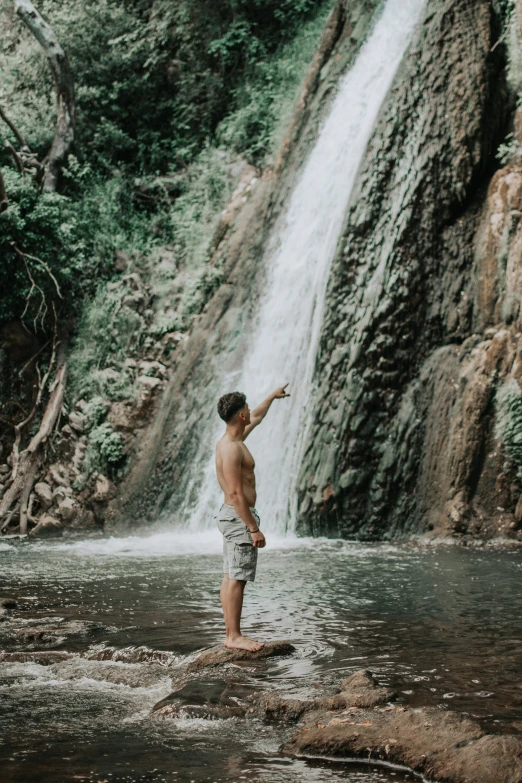 a man standing in front of a waterfall and pointing to the sky