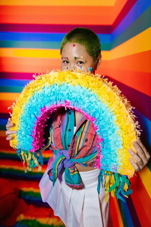 a girl in colorful clothing holding a rainbow colored pinata