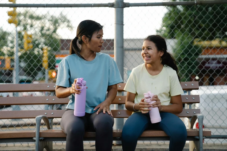 two woman sit on a bench talking to each other