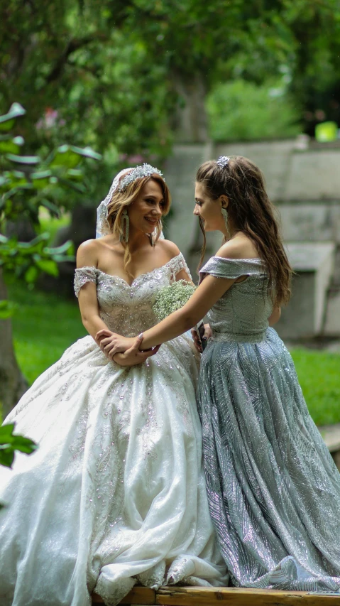 two brides in dress and tiaras are looking each other