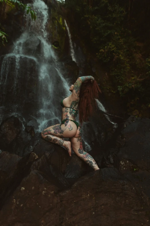 a woman in bikini and tattoo standing next to a waterfall