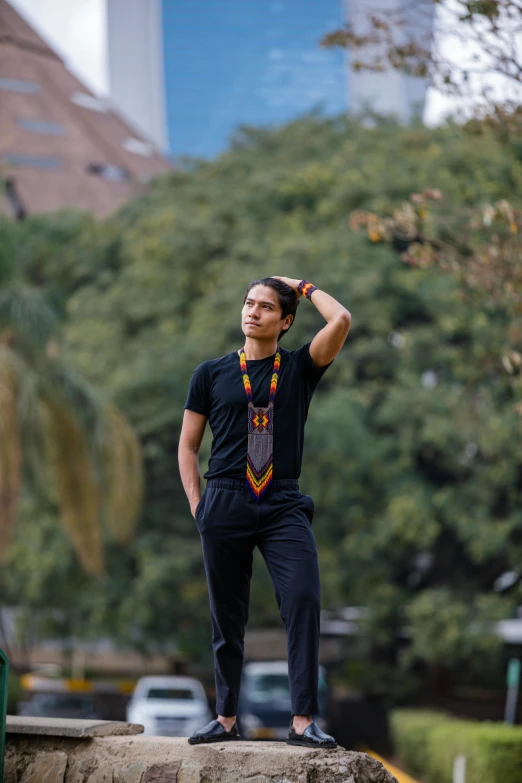 man in a shirt and pants stands on a ledge with his hands behind his head