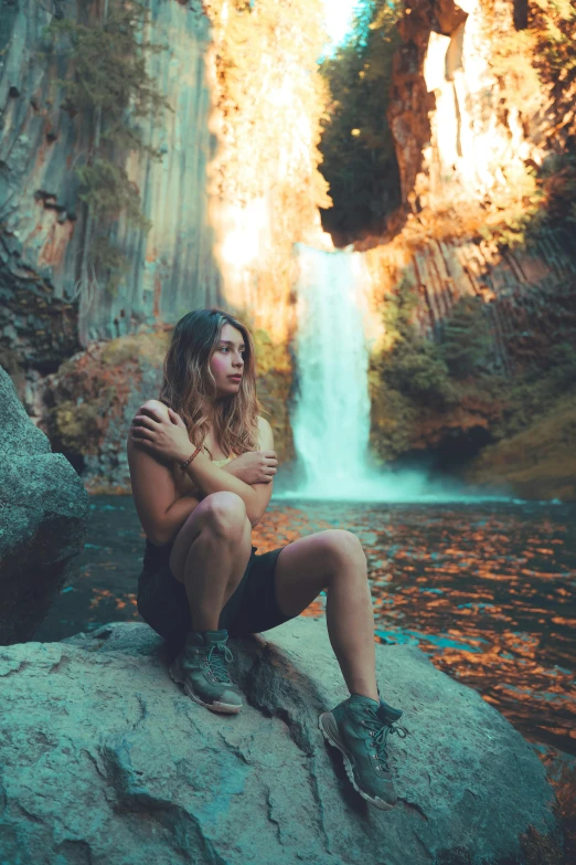 a woman sitting on the rocks near a waterfall