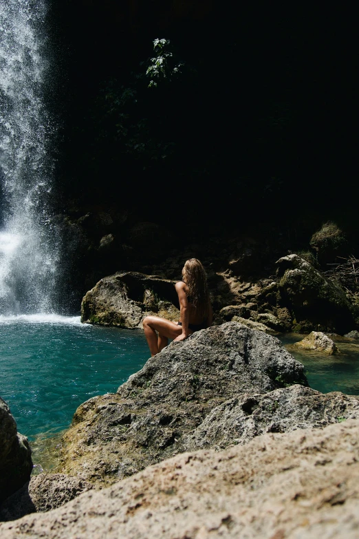 a person sitting on some rocks with a waterfall in the background