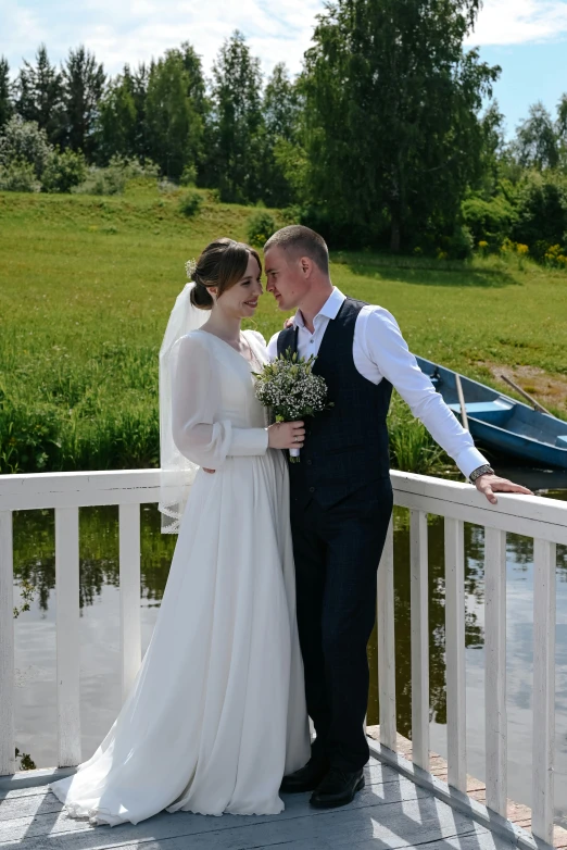 the bride and groom stand near a body of water