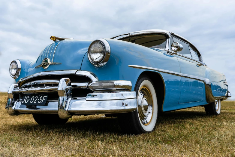 an old blue vintage car with chrome rims parked in a field