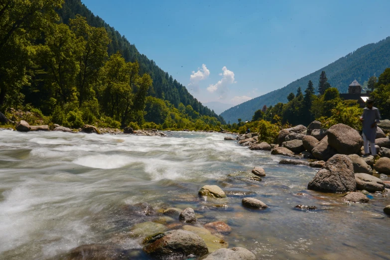 man in black standing on rocks near river with mountain view