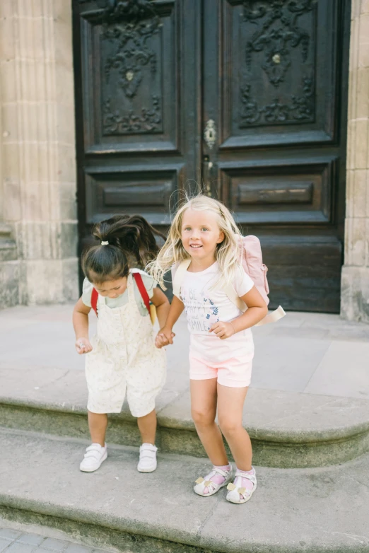 two little girls are holding hands at the front of an entrance