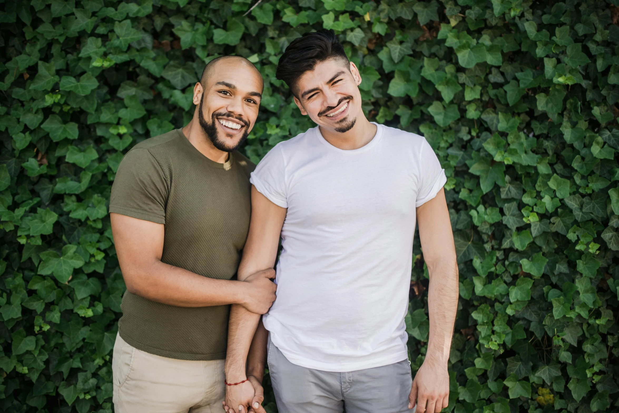 two men standing next to each other near a green hedge