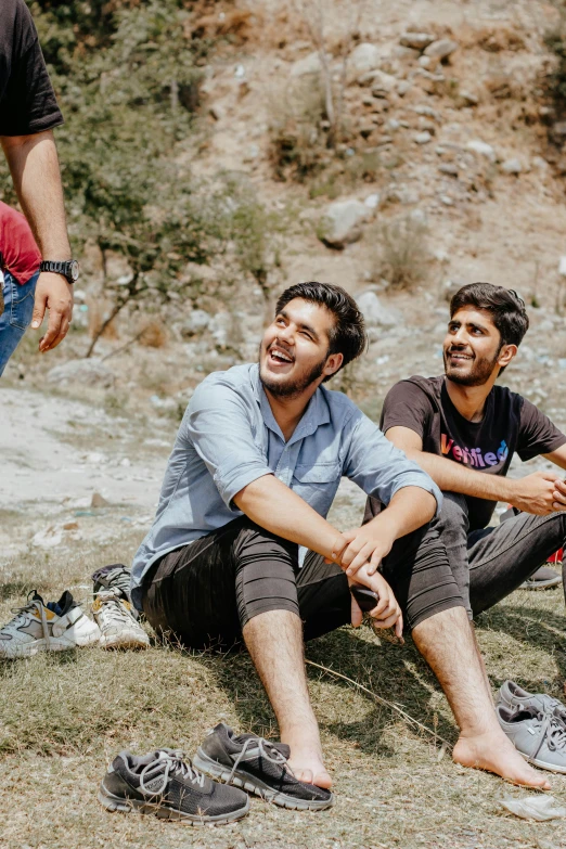 two men sitting on a hillside near their shoes