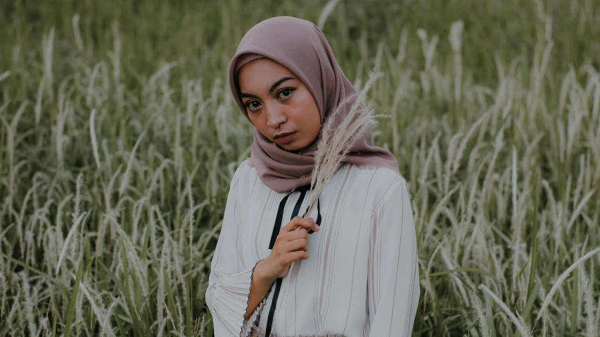 a girl in a white top is standing alone in a field of tall grass