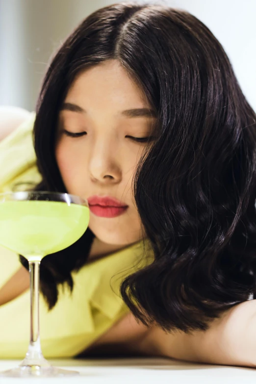 asian lady drinking green beverage from wine glass