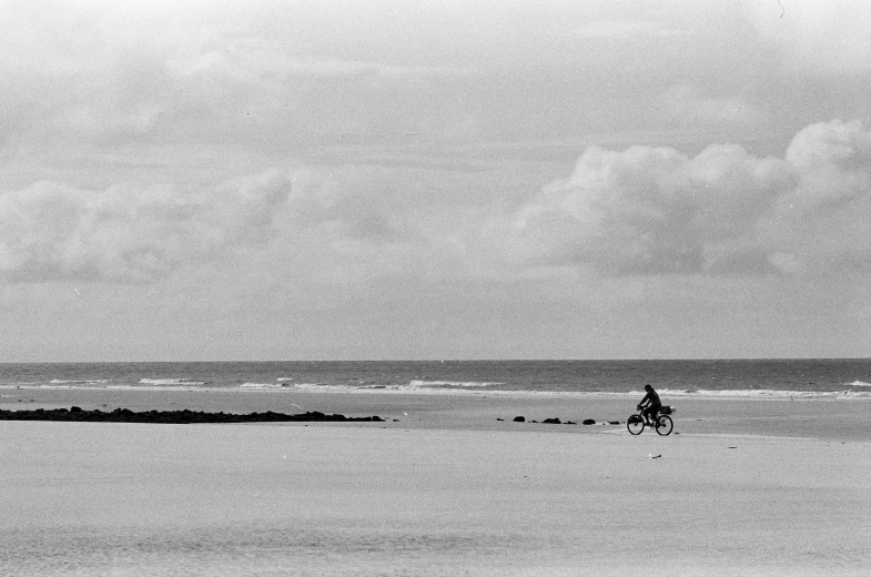 a person riding a bicycle down a beach next to the ocean