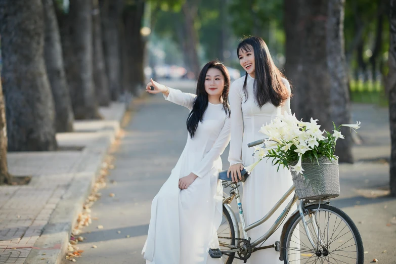 two women dressed in white posing next to a bike