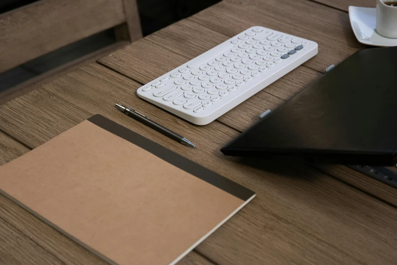 a keyboard sitting on top of a wooden table next to a notebook