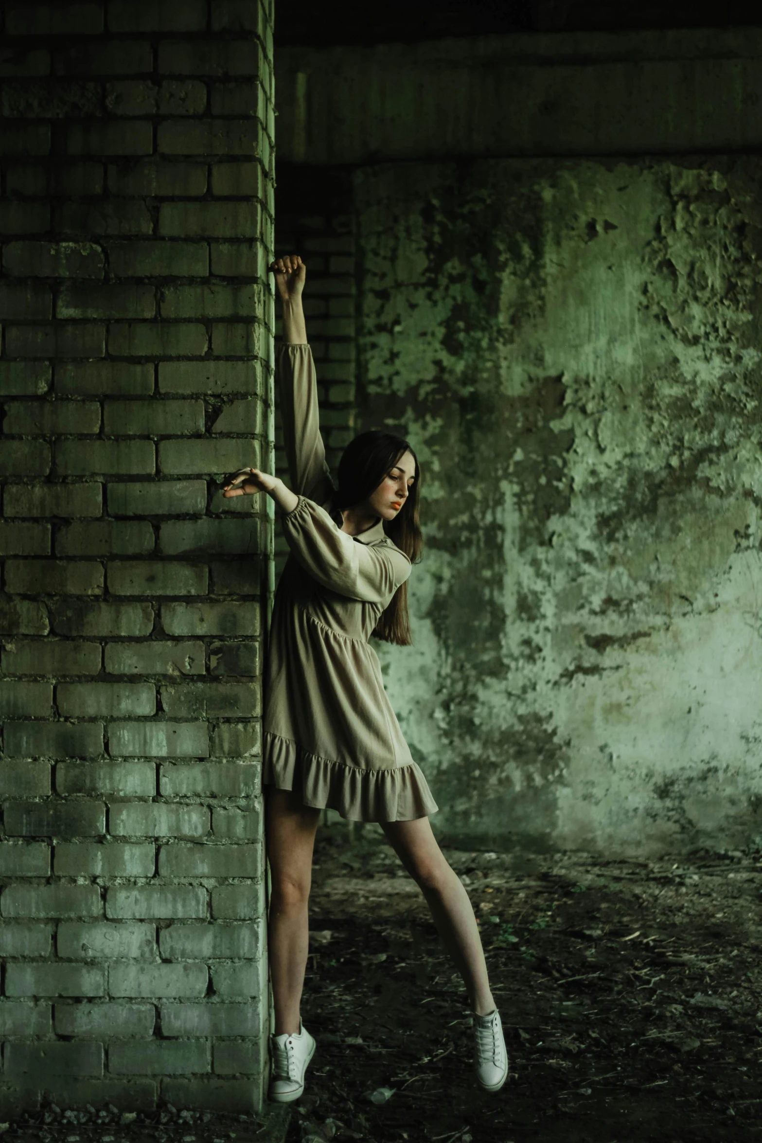 a girl with dark hair standing against a brick wall and reaching up to reach the ceiling