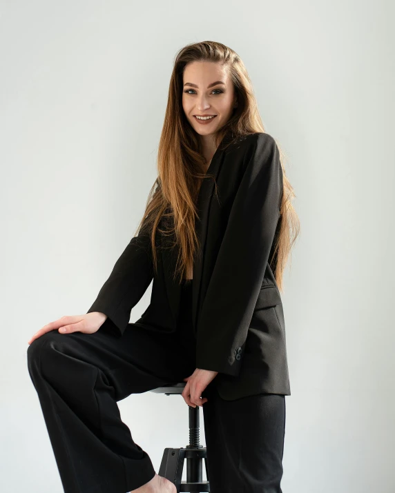 a woman in a black suit sitting on a stool