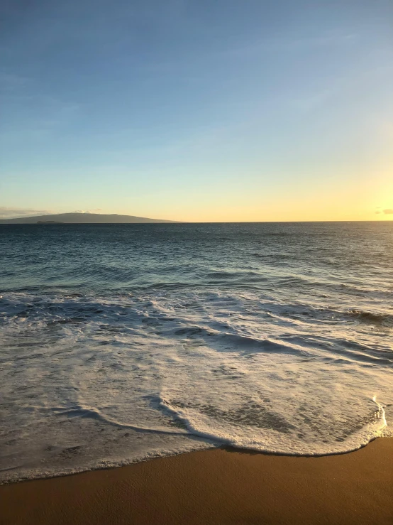 the surf of the ocean at sunrise with the sun peaking in