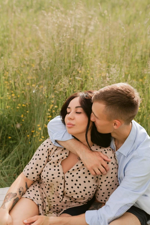 an attractive woman in brown shirt and skirt holding a man while sitting on the ground