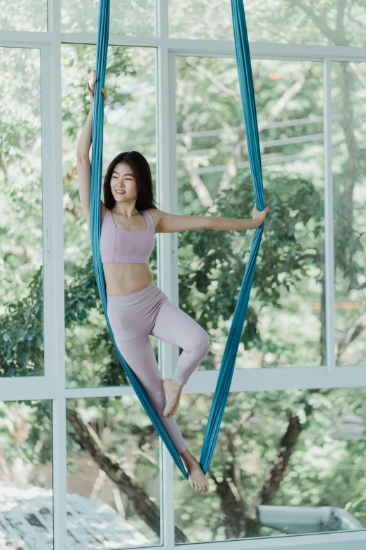 a woman sitting on top of a blue chair hanging from a window