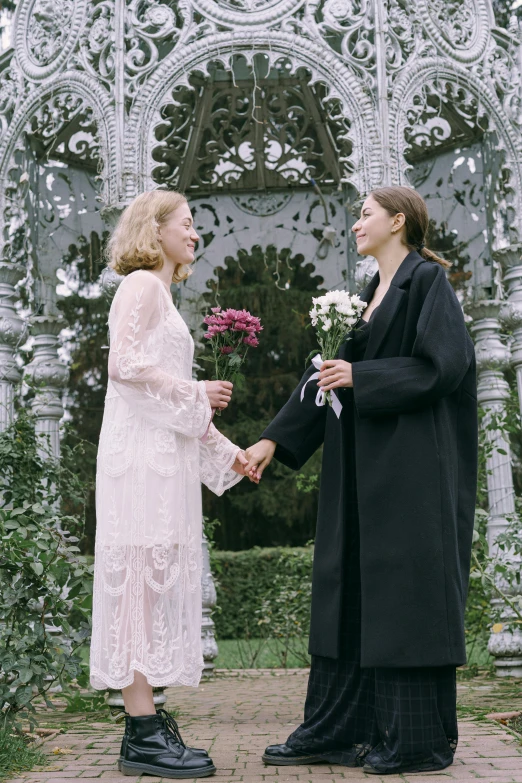 the two women are holding hands outside in front of an intricate archway