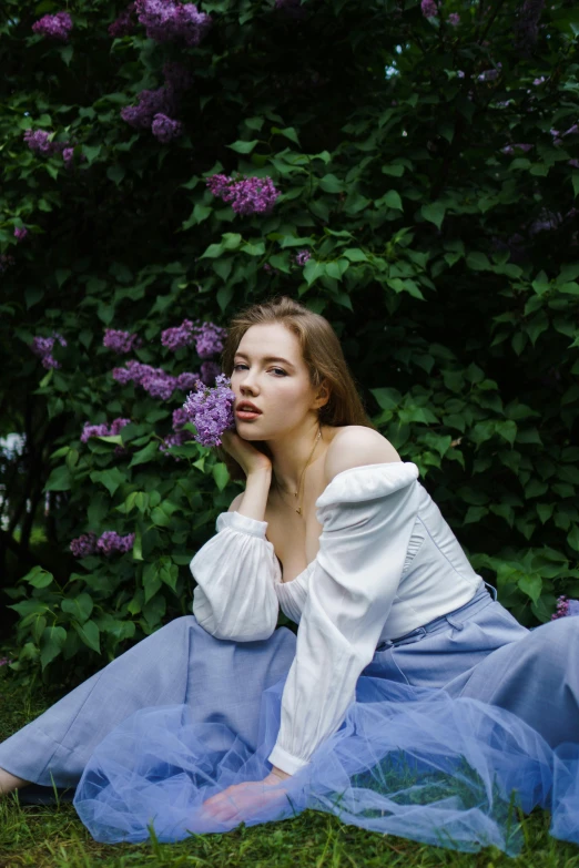 a young woman sits in the grass near purple lilacs