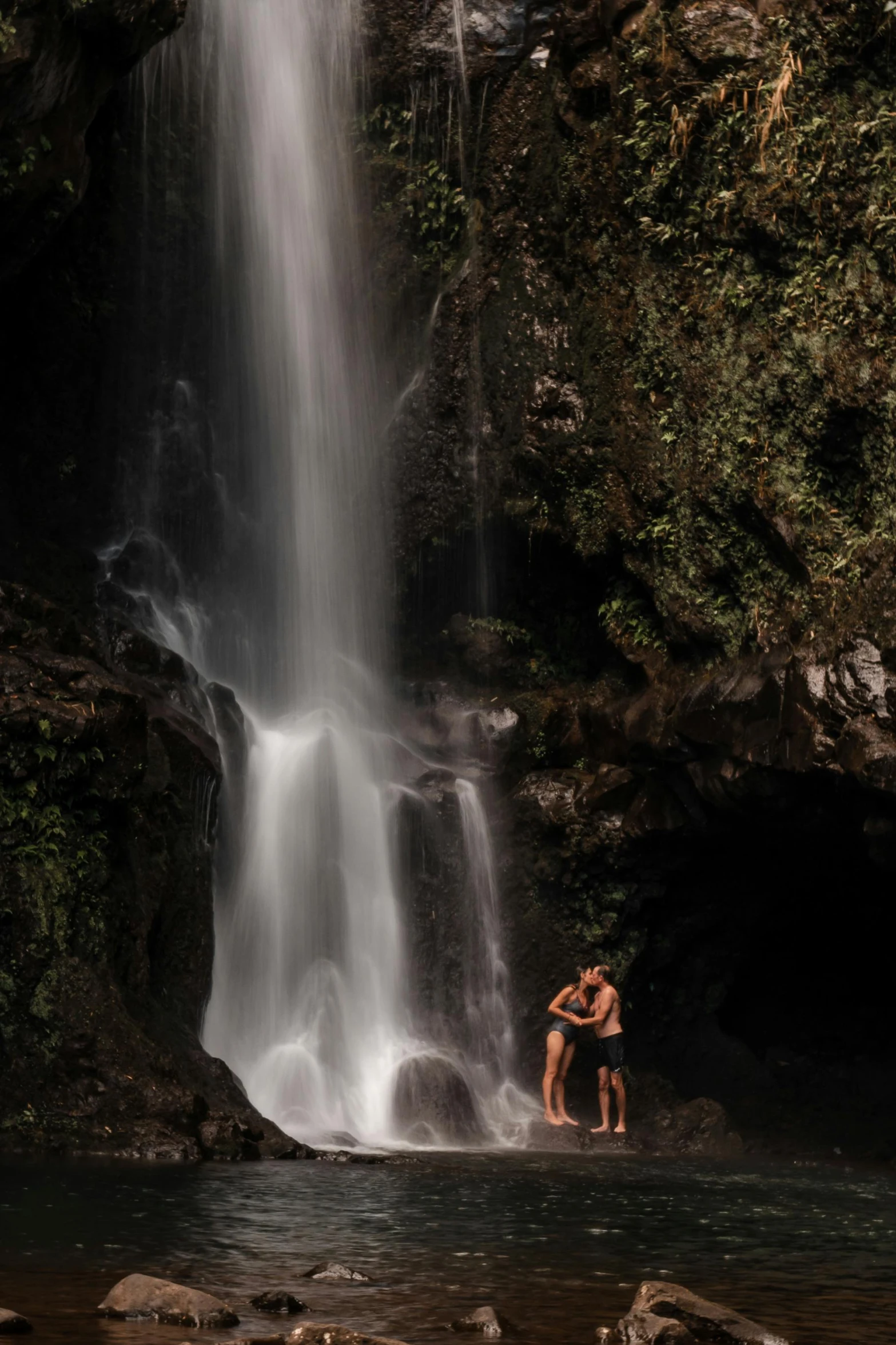 a man standing under a waterfall in the forest