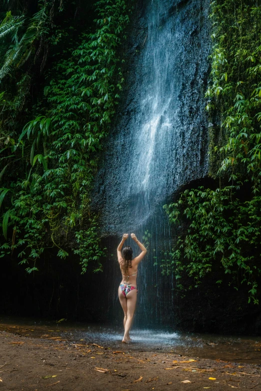 a young woman wearing a bikini splashes in front of a waterfall