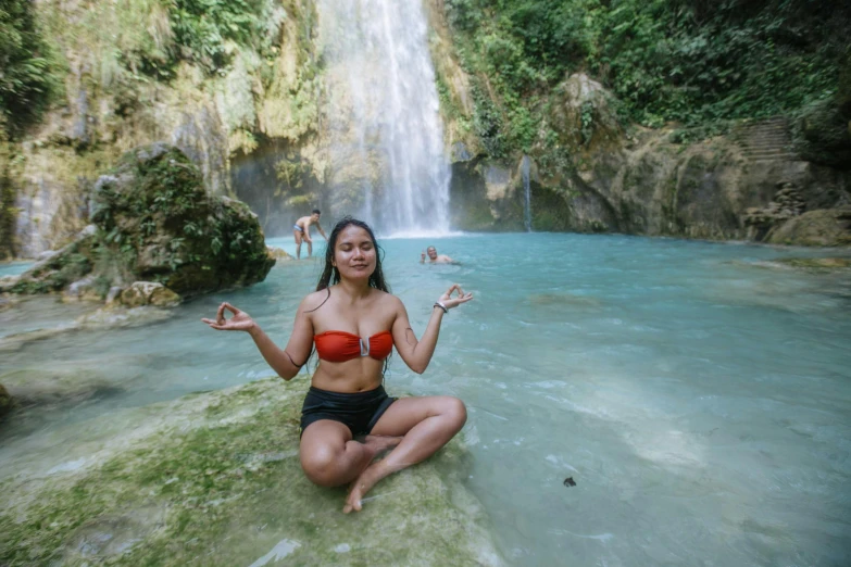 a woman sitting on the rocks in front of a waterfall