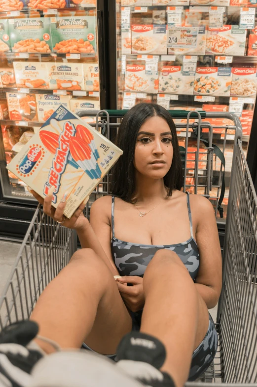 a young woman sits in a grocery cart holding an open box