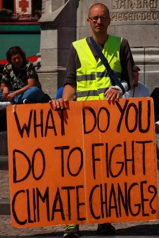 the man is holding a sign that says what do you do to fight climate change