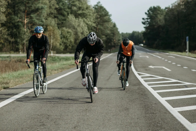 three cyclists are riding down a paved street