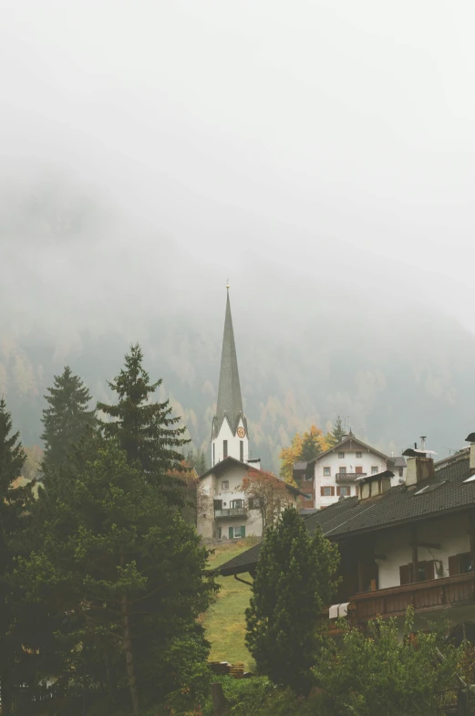 a foggy view of a building on a hillside with trees in the foreground