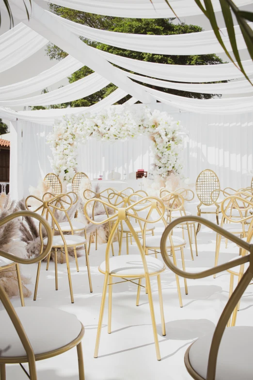 a white wedding reception with gold and ivory chairs and hanging flowers