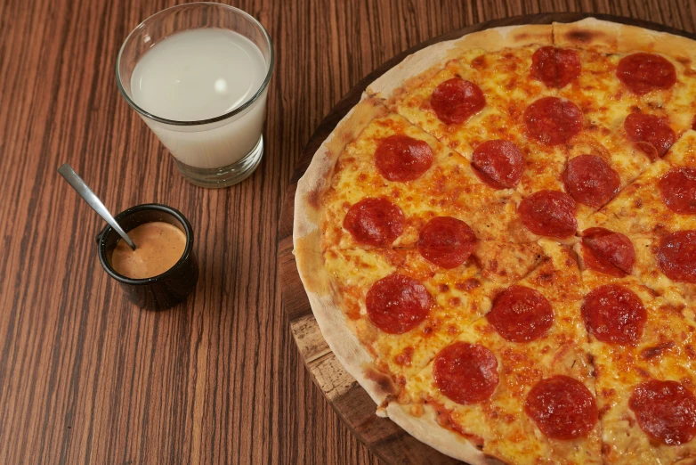 a full pepperoni pizza next to a glass of milk