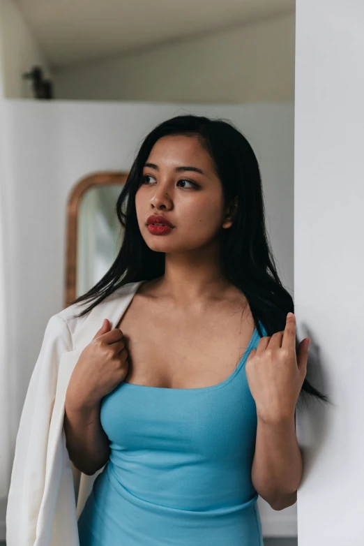 a woman in a blue top and jacket stands against a wall