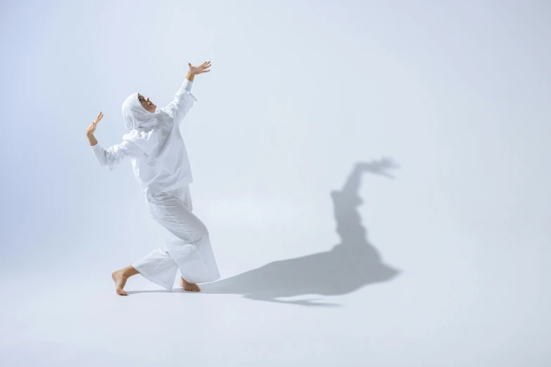 a man in white jumpsuit with his hands up and shadow on the ground