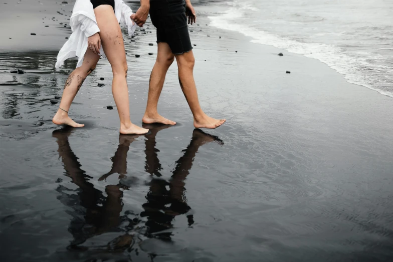 there are people walking on the beach and one person wearing black has her legs up