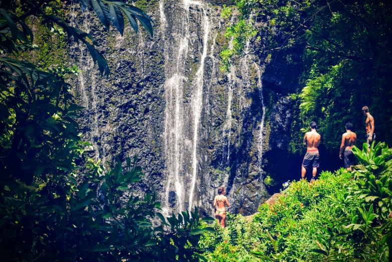 two guys are on the rock looking up at a large waterfall