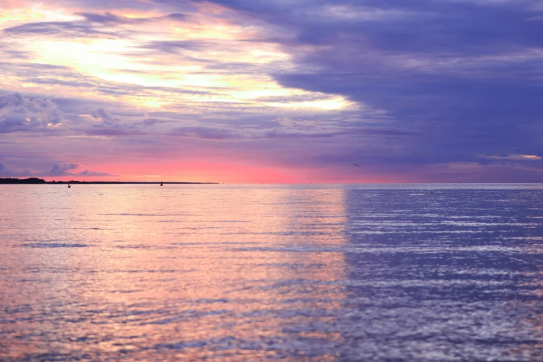 some clouds in the distance over water with a sailboat on it