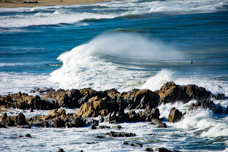 a large wave cresting over some rocks on the beach