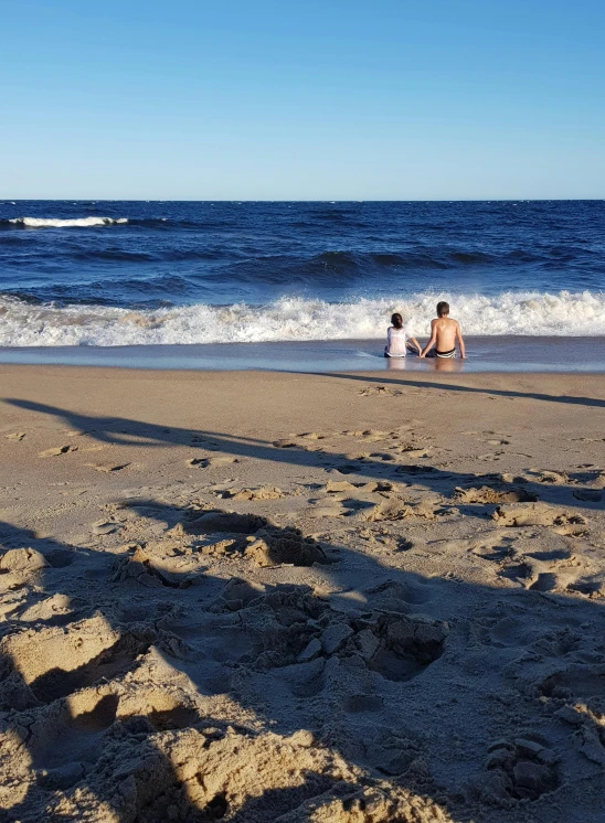 two people sit on the beach near the waves