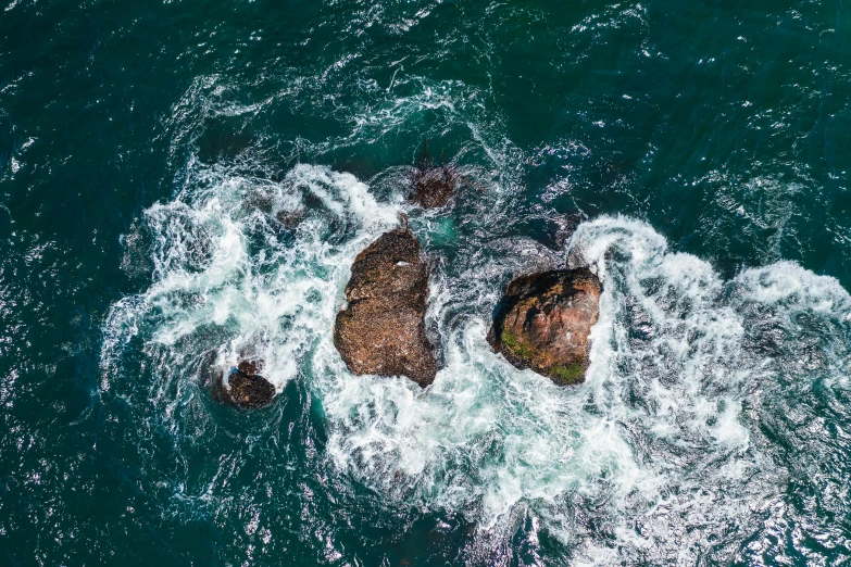 aerial view of waves splashing around rocks on top of water