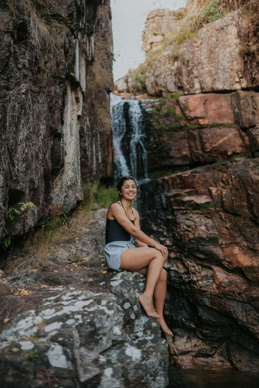 a girl sitting on a rock by the edge of a waterfall