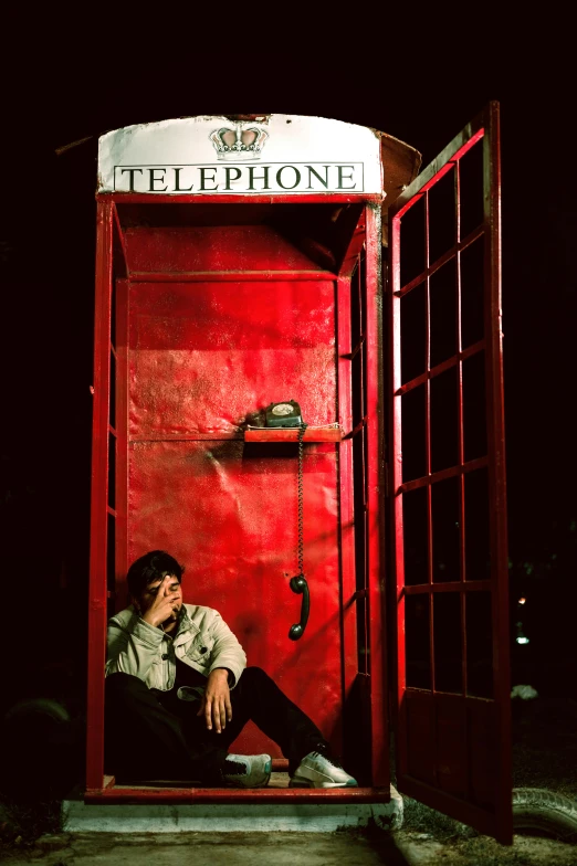 a man sitting inside a red phone booth