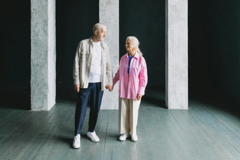 an elderly couple holds hands as they stand in an empty room