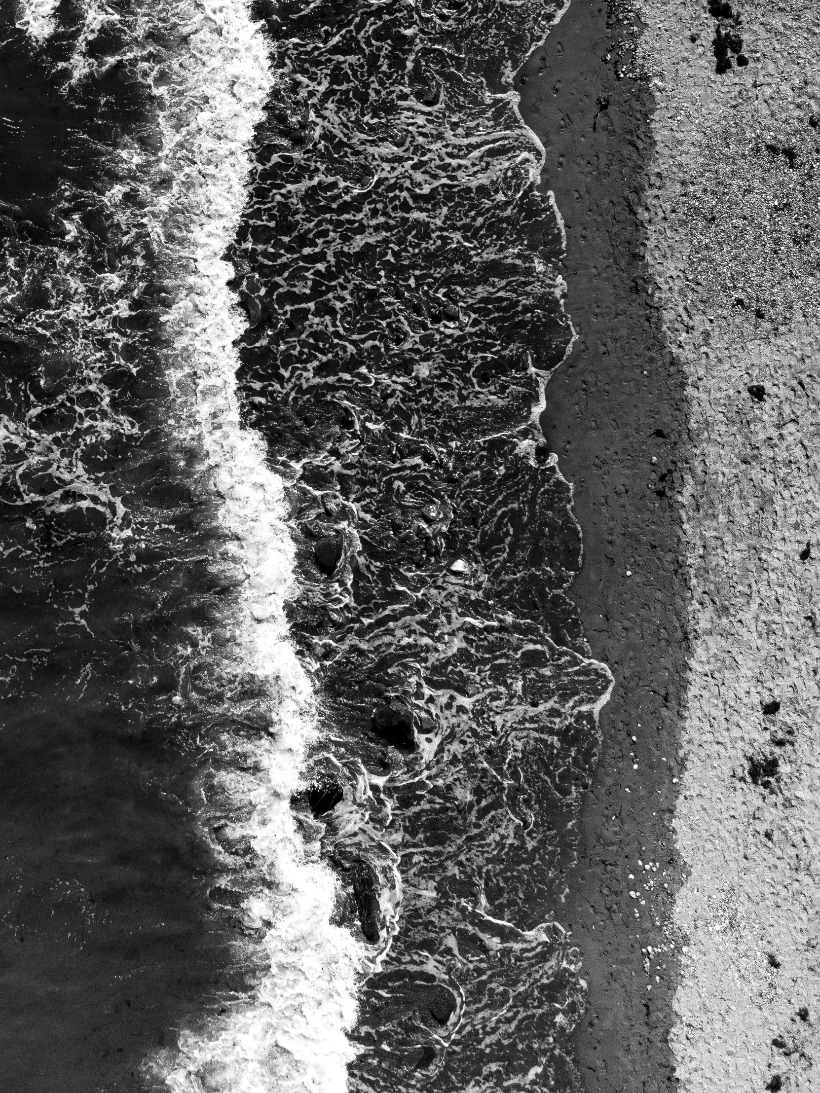 black and white po of water on the sand near beach