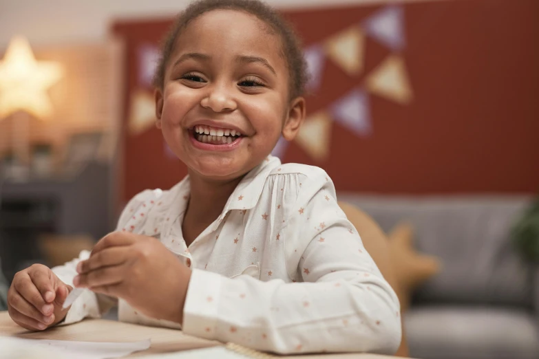 a little girl is sitting down at the table and smiling