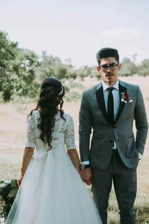 a young couple pose together in a field, wearing suits and ties